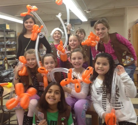 A group of girls smiling and posing with orange balloon animals