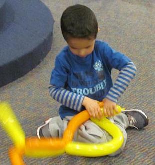 A child sits on the floor, focused on twisting colorful balloon shapes