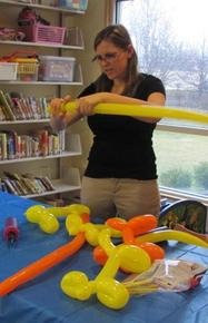 A woman twists colorful balloons into shapes at a library event