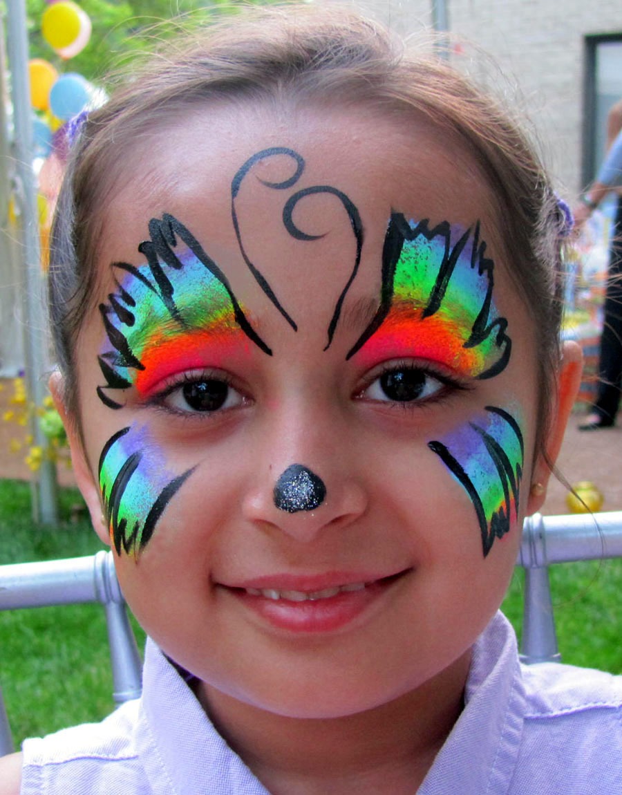 A girl with colorful butterfly face paint smiles at a festive outdoor event