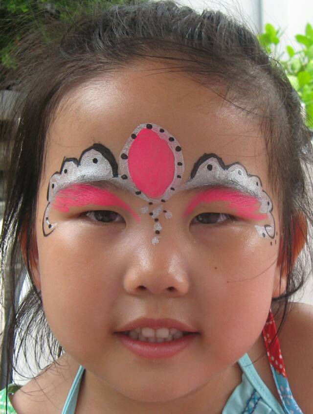 Young girl with colorful face paint, featuring pink and silver designs