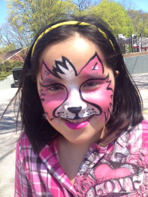 A young girl with pink and white face paint resembling a cat