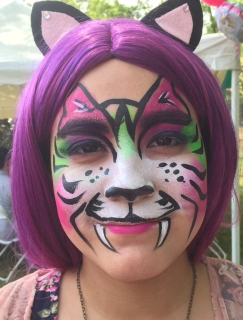 Girl with vibrant purple hair and face painted as a colorful tiger